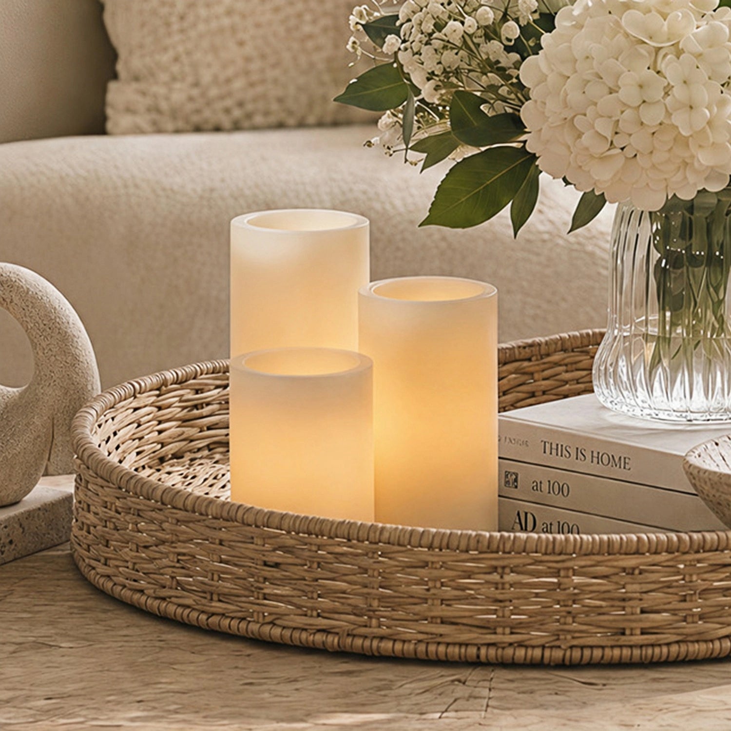 Decorative setting with candles on a woven tray, books, and flowers in a vase.#color_white