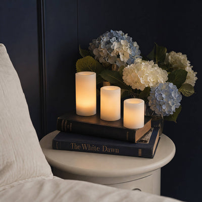 Candle holder with three candles and a bouquet of flowers on a nightstand next to a bed.