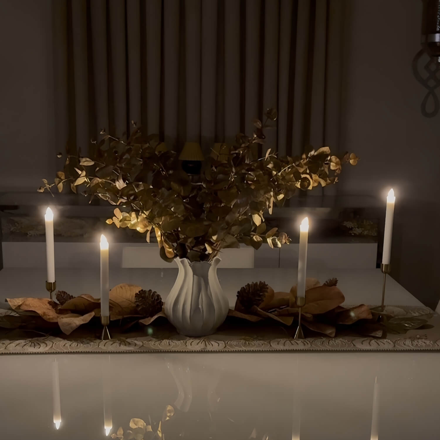 Decorative table setting with candles and a vase of flowers in a dimly lit room.