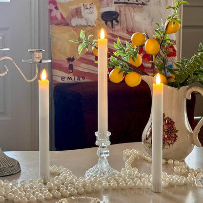 Decorative setup with candles, a crystal candlestick, and a teapot on a table.