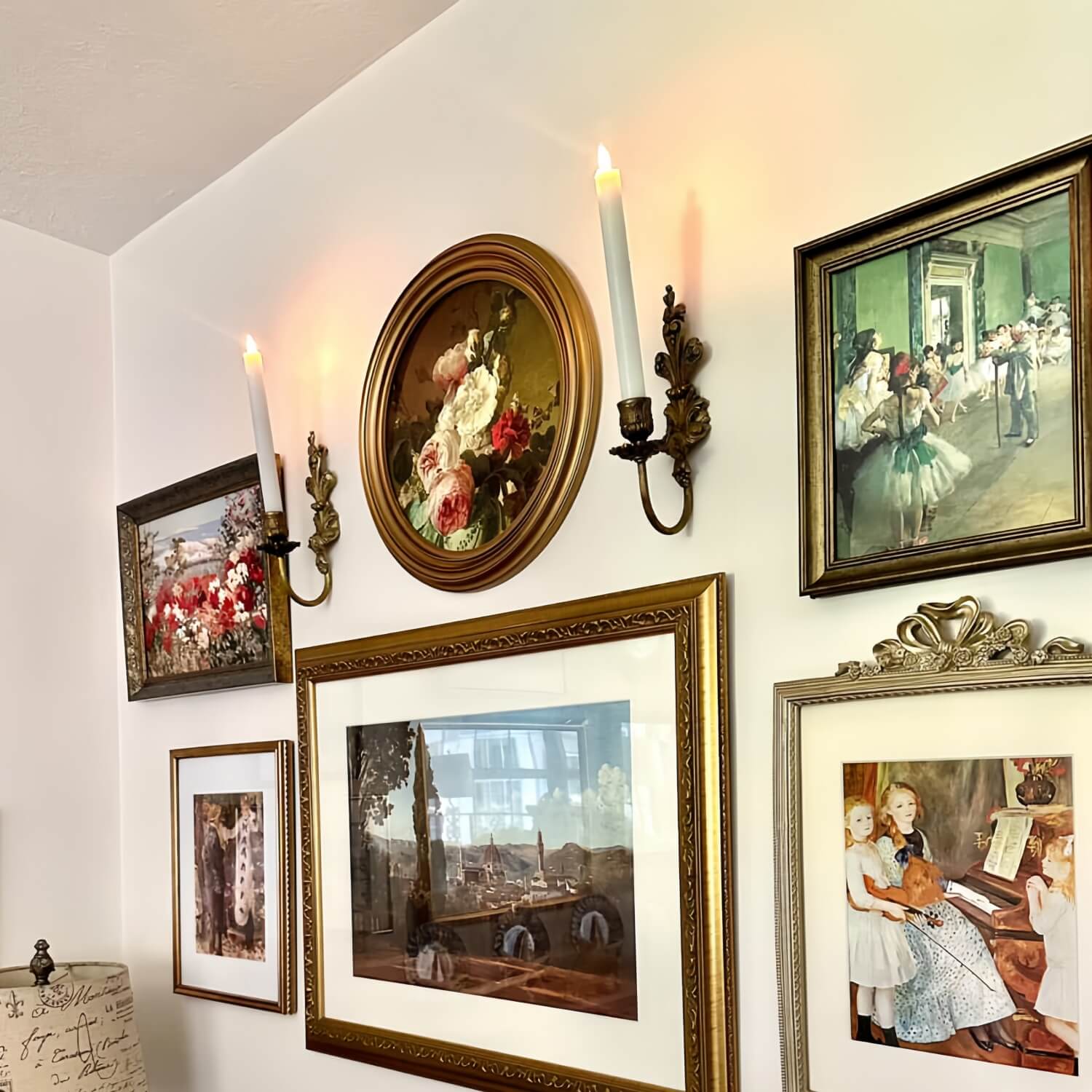Wall with various framed paintings and a lit candle