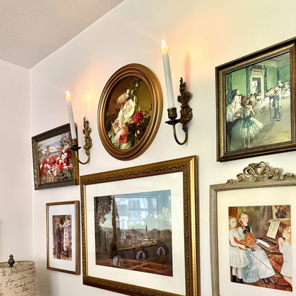Wall with various framed paintings and a lit candle