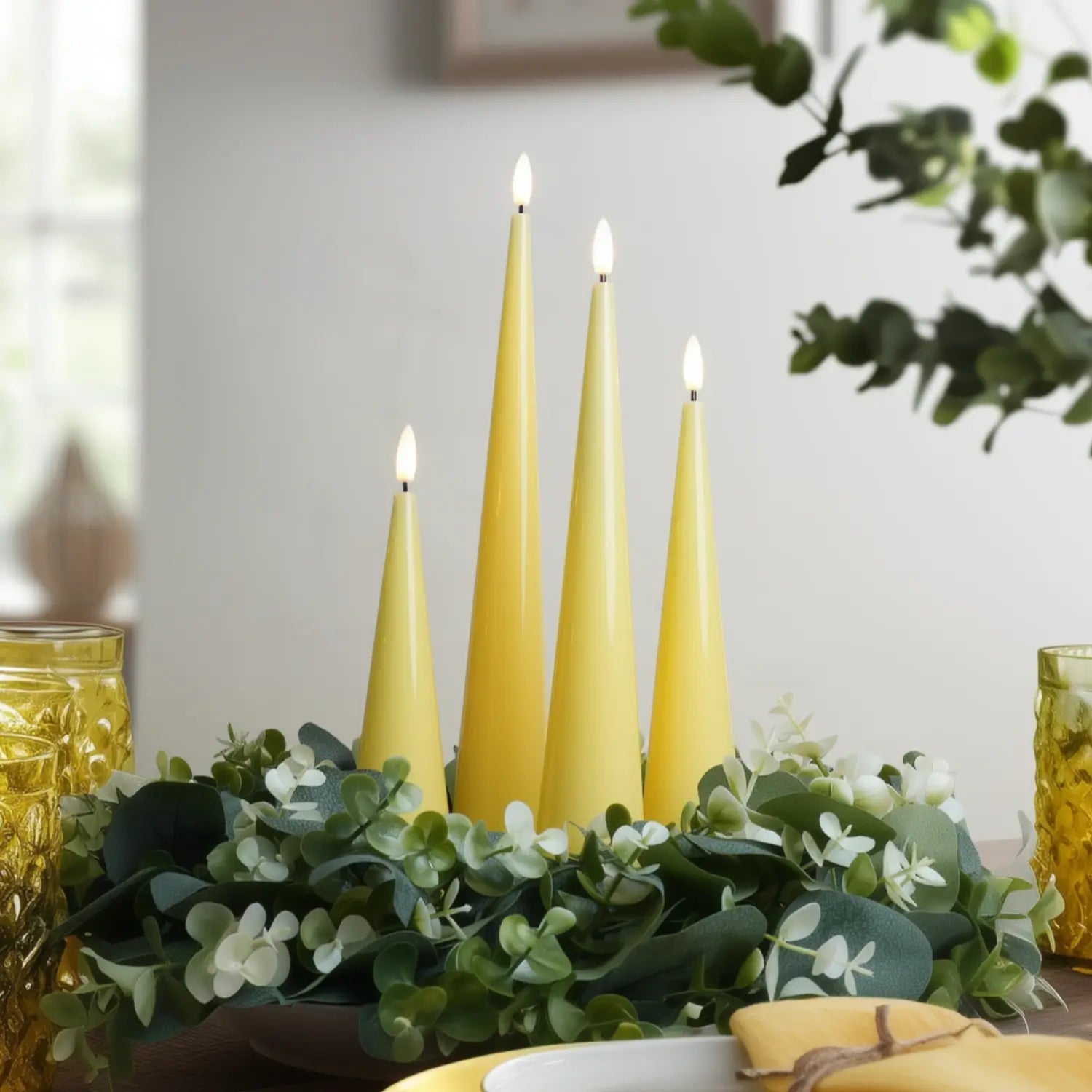 Three yellow candles on a table with greenery and a blurred background