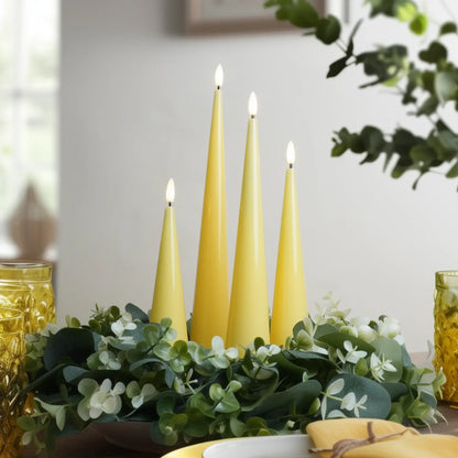 Three yellow candles on a table with greenery and a blurred background
