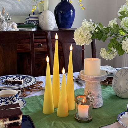 Set of four yellow taper candles on a wooden surface with a neutral background