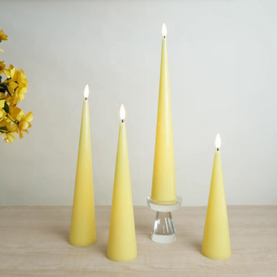 Set of four yellow taper candles on a wooden surface with a neutral background