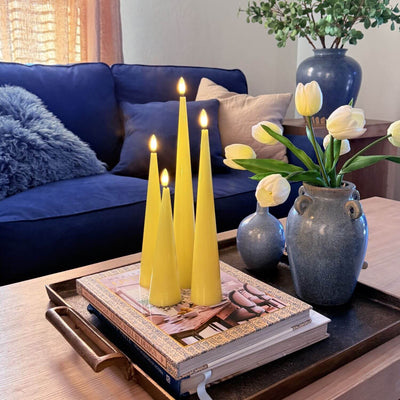 Set of four yellow taper candles on a wooden surface with a neutral background