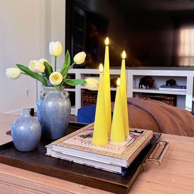 Set of four yellow taper candles on a wooden surface with a neutral background