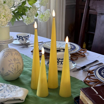 Set of four yellow taper candles on a wooden surface with a neutral background